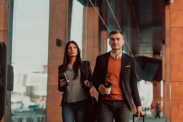 Business man and business woman talking and holding luggage traveling on a business trip, carrying fresh coffee in their hands.Business concept — стоковое фото