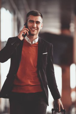 Havaalanına geldi. Erkek Gezgin, bavulunu açık havada gezdiriyor ve akıllı telefon kullanıyor. Yüksek kaliteli fotoğraf.