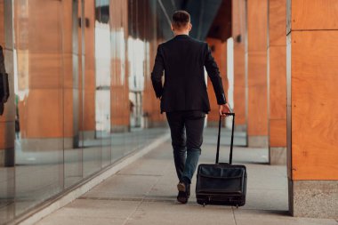 Havaalanına geldi. Erkek Gezgin, bavulunu açık havada gezdiriyor ve akıllı telefon kullanıyor. Yüksek kaliteli fotoğraf.