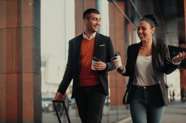 İş adamı ve iş kadını konuşuyor ve bavullarını tutuyor iş seyahatinde, ellerinde taze kahve taşıyorlar. İş konsepti. Yüksek kaliteli fotoğraf.