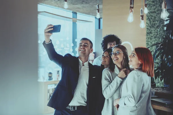 Grupa wesołych kolegów robi sobie selfie i gestykuluje stojąc w nowoczesnym biurze. — Zdjęcie stockowe