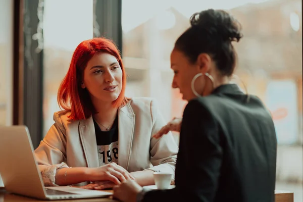Deux jeunes femmes d'affaires assises à table dans un café. Fille montre des informations de collègue sur l'écran d'ordinateur portable. Fille en utilisant smartphone, blogging. Travail d'équipe, réunion d'affaires. — Photo