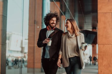 İki kişi işe ara verip kahve içtikleri modern bir şirketin önünde yürüyor..