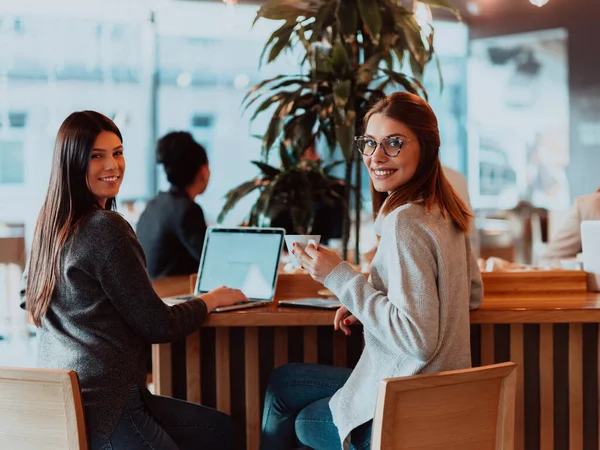 Duas jovens empresárias sentadas à mesa no café. Menina mostra informações colega na tela do laptop. Menina usando smartphone, blogging. Trabalho em equipe, reunião de negócios.. — Fotografia de Stock