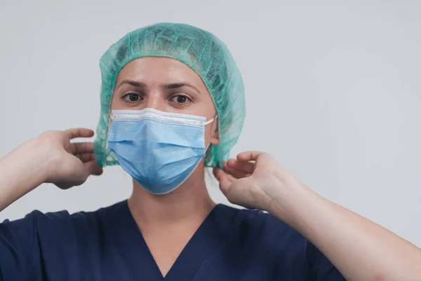 Primer plano de doctora o científica con máscara médica y gorra quirúrgica sobre fondo gris. Ella está ajustando la máscara con —  Fotos de Stock