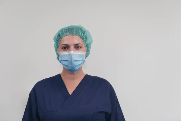 Close up of female doctor or scientist with a medical mask and surgical cap over grey background. She is adjusting mask with — Stock Photo, Image