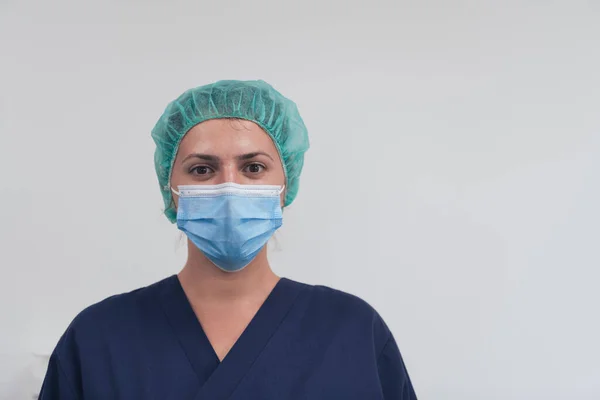 Close up of female doctor or scientist with a medical mask and surgical cap over grey background. She is adjusting mask with — Stock Photo, Image