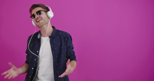 Homem dançando e sorrindo sobre fundo de cor enquanto ouve música — Vídeo de Stock