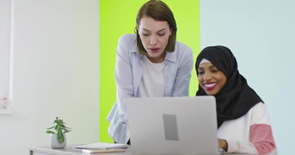 多様性多民族女性会議事務所で。Hijabで働く笑顔の女の子ノートパソコンで,ブロンドは、画面を見て. — ストック動画