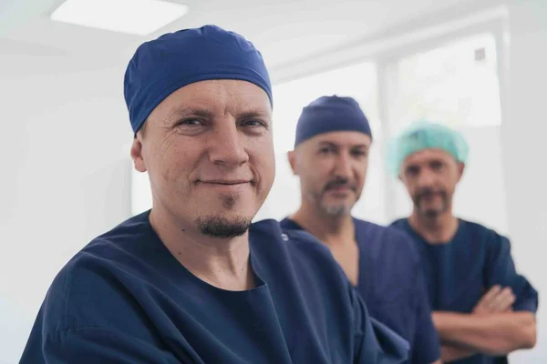 Többnemzetiségű ortopéd orvos az orvosi csapata előtt, aki arcmaszkot viselő kamerát néz. — Stock Fotó
