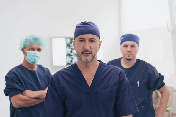 Médico ortopédico multiétnico frente a su equipo médico mirando a la cámara con máscara facial —  Fotos de Stock