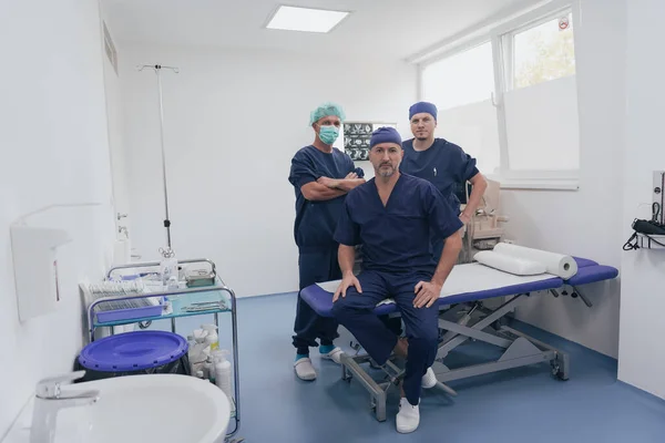 Çok ırklı ortopedi doktoru tıbbi ekibinin önünde yüz maskesi takmış kameraya bakıyor. — Stok fotoğraf