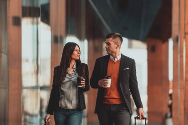 Elinde bavul olan iş adamı, iş arkadaşıyla şehirde dolanıp kahve içiyor.