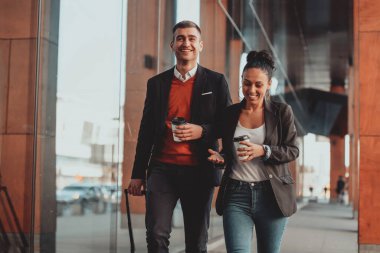 İş adamı ve iş kadını konuşuyor ve bavullarını tutuyor iş seyahatinde, ellerinde taze kahve taşıyorlar. İş konsepti. Yüksek kaliteli fotoğraf.