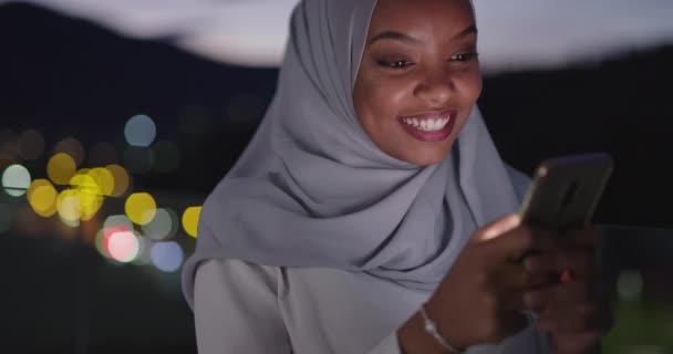 在城市街道上 年轻的穆斯林妇女夜晚戴着围巾面纱 用智能手机发短信 背景为城市灯火通明 — 图库视频影像