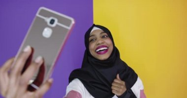 Cep telefonuyla tesettürlü mutlu siyah Arap kadın arka planda selfie çekiyor.