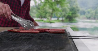 Barbekü ızgarasında nefis yemekler pişiren adam doğada güzel bir yaz akşamında nehrin kenarında Fransız yemeği partisi veriyor.
