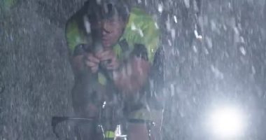 Triatlon atleti, yağmurlu bir karanlıkta yoğun bir idmanda profesyonel bir yarış bisikletine biniyor. Yağmurlu bir gecede kötü hava koşullarında antrenman ya da yarışma. Ağır çekim. Merhaba kaliteli 4K görüntüler
