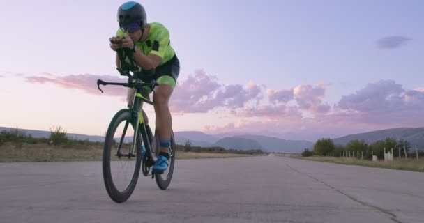 プロのレーシングバイクに乗ってトライアスロン選手の夜の自転車トレーニング 夕方には曲がりくねった田舎道で健康的な強烈なワークアウト スローモーショントラッキングショット — ストック動画