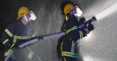 İtfaiyeci erkek ve kadın grup acil bir durumda alevlerle savaşmak için su kullanıyor. İtfaiyeci ekibi yangın geçirmez ekipmanla gece eğitiminde itfaiye aracının yanında. Yavaş çekim. 