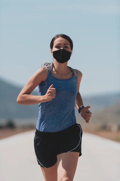 Entschlossene Fitness-Frau in kurzer Kleidung mit roter Schutzmaske, die während des Coronavirus-Ausbruchs in der Stadt im Freien läuft. Covid 19 und körperliche Joggingaktivität, Sport und Fitness. — Stockfoto