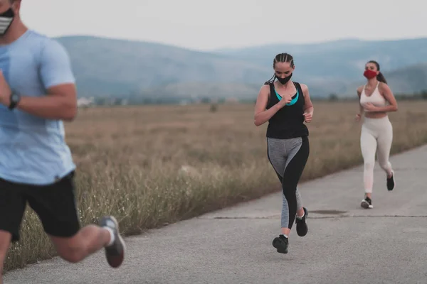Drei multiethnische Läuferinnen tragen Gesichtsmasken und halten die soziale Distanz im Freien. Fit gesundes, vielfältiges Team trägt Sportbekleidung Joggen im Park auf Natursportpfad zur Sicherheit. — Stockfoto