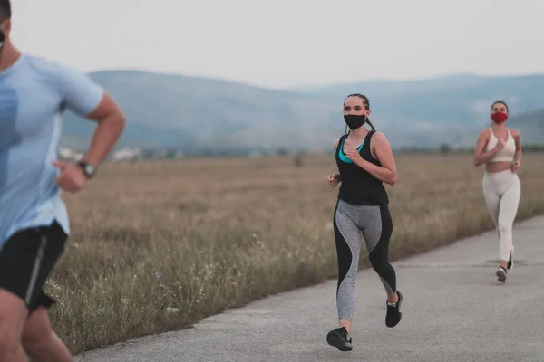 Tre multietniska kvinnor löpare grupp bära ansiktsmasker kör hålla sociala avstånd utomhus. Passform hälsosam mångfald team bär sportkläder jogging i parken på natur sport spår distans för säkerhet. — Stockfoto