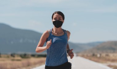 Coronavirus salgını sırasında şehirde koşan kısa elbiseli, kırmızı koruyucu maskeli bir kadın. Covid 19 ve fiziksel koşu aktivitesi, spor ve spor.