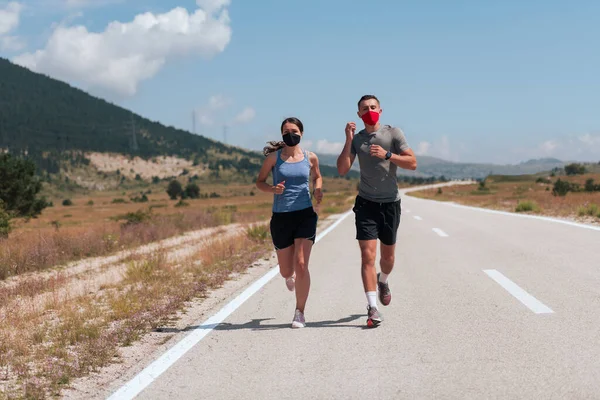 Ung man och kvinna i skyddsmasker springer och gör övningar utomhus på morgonen. Sport, Aktivt liv Jogging under karantän. Covid-19 ny normal. Selektiv inriktning. — Stockfoto