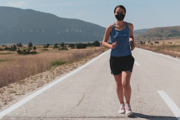 Entschlossene Fitness-Frau in kurzer Kleidung mit roter Schutzmaske, die während des Coronavirus-Ausbruchs in der Stadt im Freien läuft. Covid 19 und körperliche Joggingaktivität, Sport und Fitness. — Stockfoto