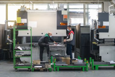 Koronavirüs salgınından dolayı koruyucu maske takan iki işçi modern bir fabrikada çalışıyor ve CNC makinesi için program ve materyal hazırlıyorlar. Yüksek kalite fotoğraf