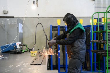 Modern metal üretim ve işleme endüstrisinde çalışan bir kadın ürünü kaynak yaparak CNC makinesine hazırlıyor. Yüksek kalite fotoğraf