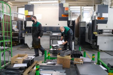 Koronavirüs salgınından dolayı koruyucu maske takan iki işçi modern bir fabrikada çalışıyor ve CNC makinesi için program ve materyal hazırlıyorlar. Yüksek kalite fotoğraf