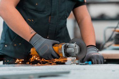Heavy Industry Engineering Factory Interior with Industrial Worker Using Angle Grinder and Cutting a Metal Tube. Güvenlik Üniforması ve Sert Şapka Üretim Metal Yapıları Müteahhiti. Yüksek kalite