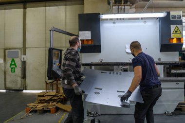 Koronavirüs salgınından dolayı koruyucu maske takan iki işçi modern bir fabrikada çalışıyor ve CNC makinesi için program ve materyal hazırlıyorlar. Yüksek kalite fotoğraf