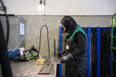 Modern metal üretim ve işleme endüstrisinde çalışan bir kadın ürünü kaynak yaparak CNC makinesine hazırlıyor. Yüksek kalite fotoğraf