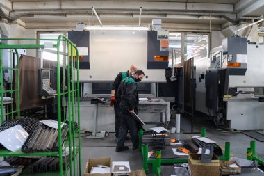 Koronavirüs salgınından dolayı koruyucu maske takan iki işçi modern bir fabrikada çalışıyor ve CNC makinesi için program ve materyal hazırlıyorlar. Yüksek kalite fotoğraf