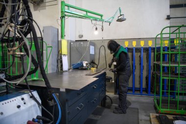 Modern metal üretim ve işleme endüstrisinde çalışan bir kadın ürünü kaynak yaparak CNC makinesine hazırlıyor. Yüksek kalite fotoğraf