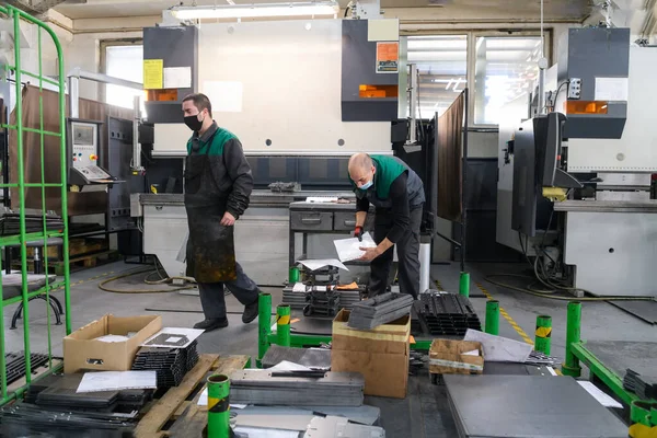 Koronavirüs salgınından dolayı koruyucu maske takan iki işçi modern bir fabrikada çalışıyor ve CNC makinesi için program ve materyal hazırlıyorlar. Yüksek kalite fotoğraf