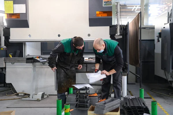 Koronavirüs salgınından dolayı koruyucu maske takan iki işçi modern bir fabrikada çalışıyor ve CNC makinesi için program ve materyal hazırlıyorlar. Yüksek kalite fotoğraf