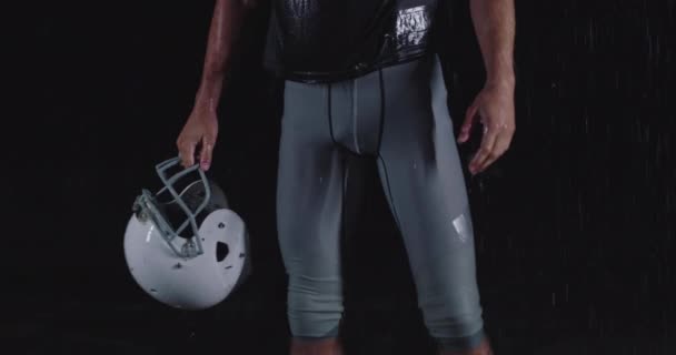 Portrait of the determined professional American football player in dark night holding the ball while rain is falling — Stok Video