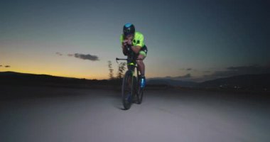 Profesyonel bir yarış bisikletine binen triatlon sporcusunun gece bisikleti eğitimi. Akşamları virajlı bir yolda sağlıklı ve yoğun bir egzersiz. Yavaş çekim izleme çekimi. 
