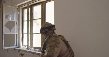 Modern savaş askeri vitrin değiştiren şarjör yakınlarında görev yapıyor ve siper alıyor. Kentsel savaş alanının penceresinden ateş etmek. Yüksek kalite 4K görüntü. Yavaş çekim. 