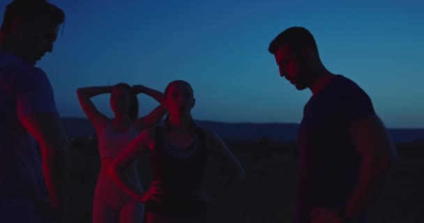 Multiethnic group of athlete resting after running in night time on a panoramic road — стоковое видео