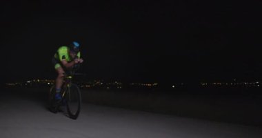 Profesyonel bir yarış bisikletine binen triatlon sporcusunun gece bisikleti eğitimi. Akşamları virajlı bir yolda sağlıklı ve yoğun bir egzersiz. Yavaş çekim izleme çekimi. 