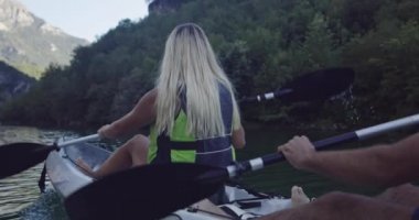 Kano yavaş çekimde kürek çekiyor. Kanocu kadın ve erkek arkadaşlarıyla güzel bir arazide kayak yapıyor. Kayakçılar gölde bir kanoyla spor yapıyorlar. Yaz boyunca su sporları. Yüksek kalite 4k görüntü