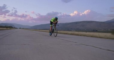 Profesyonel bir yarış bisikletine binen triatlon sporcusunun gece bisikleti eğitimi. Akşamları virajlı bir yolda sağlıklı ve yoğun bir egzersiz. Yavaş çekim izleme çekimi. 