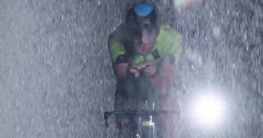 Triatlon atleti, yağmurlu bir karanlıkta yoğun bir idmanda profesyonel bir yarış bisikletine biniyor. Yağmurlu bir gecede kötü hava koşullarında antrenman ya da yarışma. Ağır çekim. Merhaba kaliteli 4K görüntüler