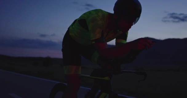プロのレーシングバイクに乗ってトライアスロン選手の夜の自転車トレーニング 夕方には曲がりくねった田舎道で健康的な強烈なワークアウト スローモーショントラッキングショット — ストック動画