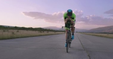 Profesyonel bir yarış bisikletine binen triatlon sporcusunun gece bisikleti eğitimi. Akşamları virajlı bir yolda sağlıklı ve yoğun bir egzersiz. Yavaş çekim izleme çekimi. 